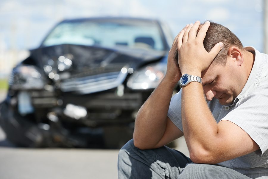man holding head in front of crashed vehicle - auto accident concept