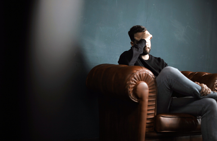 man looking sad and holding his head on a couch - depression concept