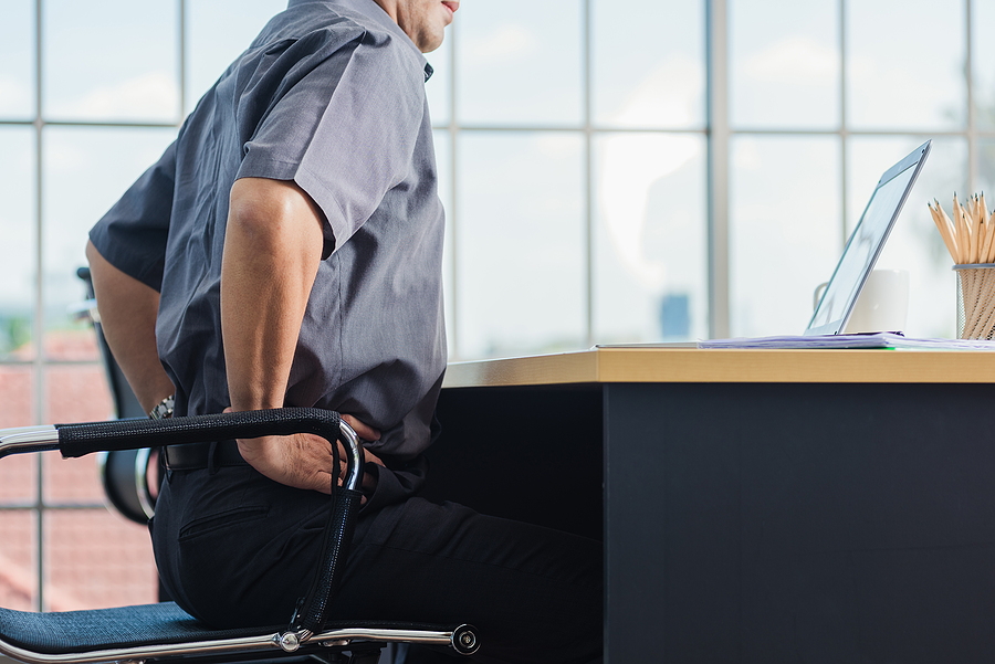 Older man sitting at desk and clutching lower back - lumbar strain concept
