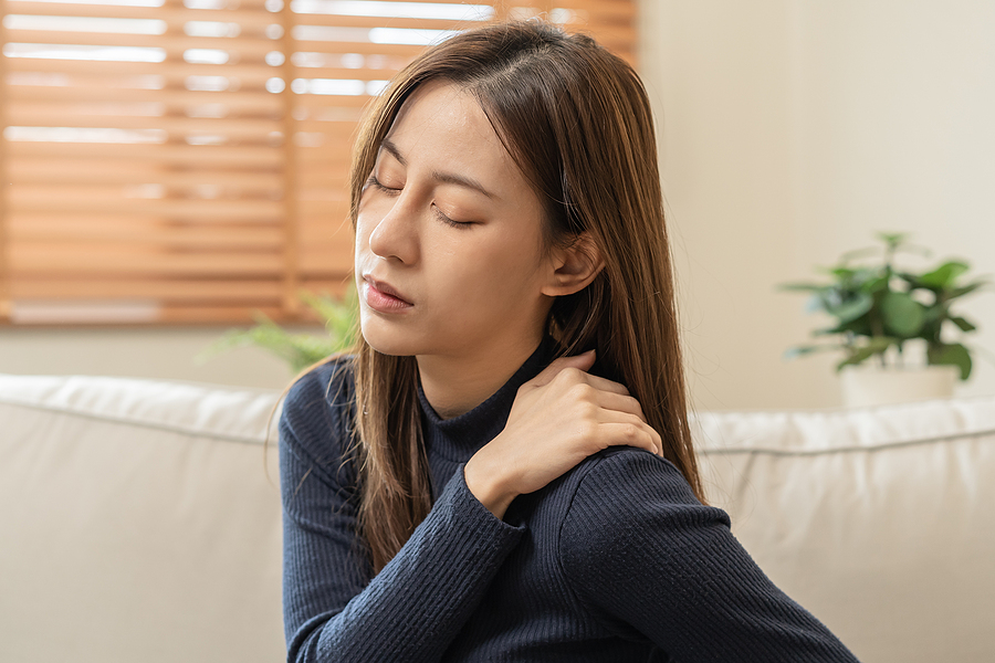 Woman sitting on a couch holding her shoulder - fibromyalgia pain concept