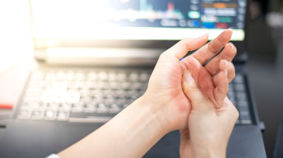 functional limitations concept - woman holding her hand in pain after typing at work