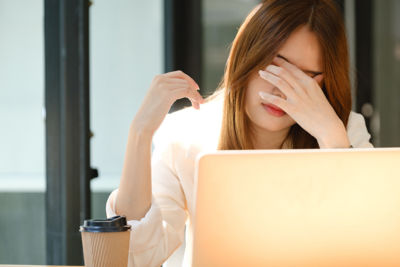 Young woman with Chronic Fatigue Syndrome (CFS) struggling to focus on her laptop - young woman rubbing her eyes with fatigue