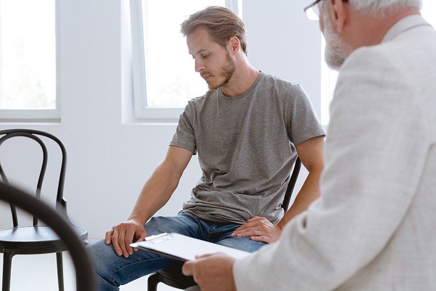 young bearded man with bipolar disorder discussing his condtiion with an older male therapist in a white coat
