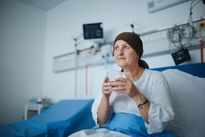 Woman with headwrap sitting in hospital room after chemotherapy treatment - cancer disability concept