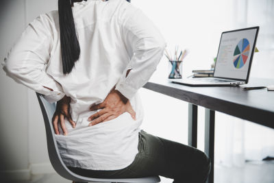 young woman at computer holding back in pain